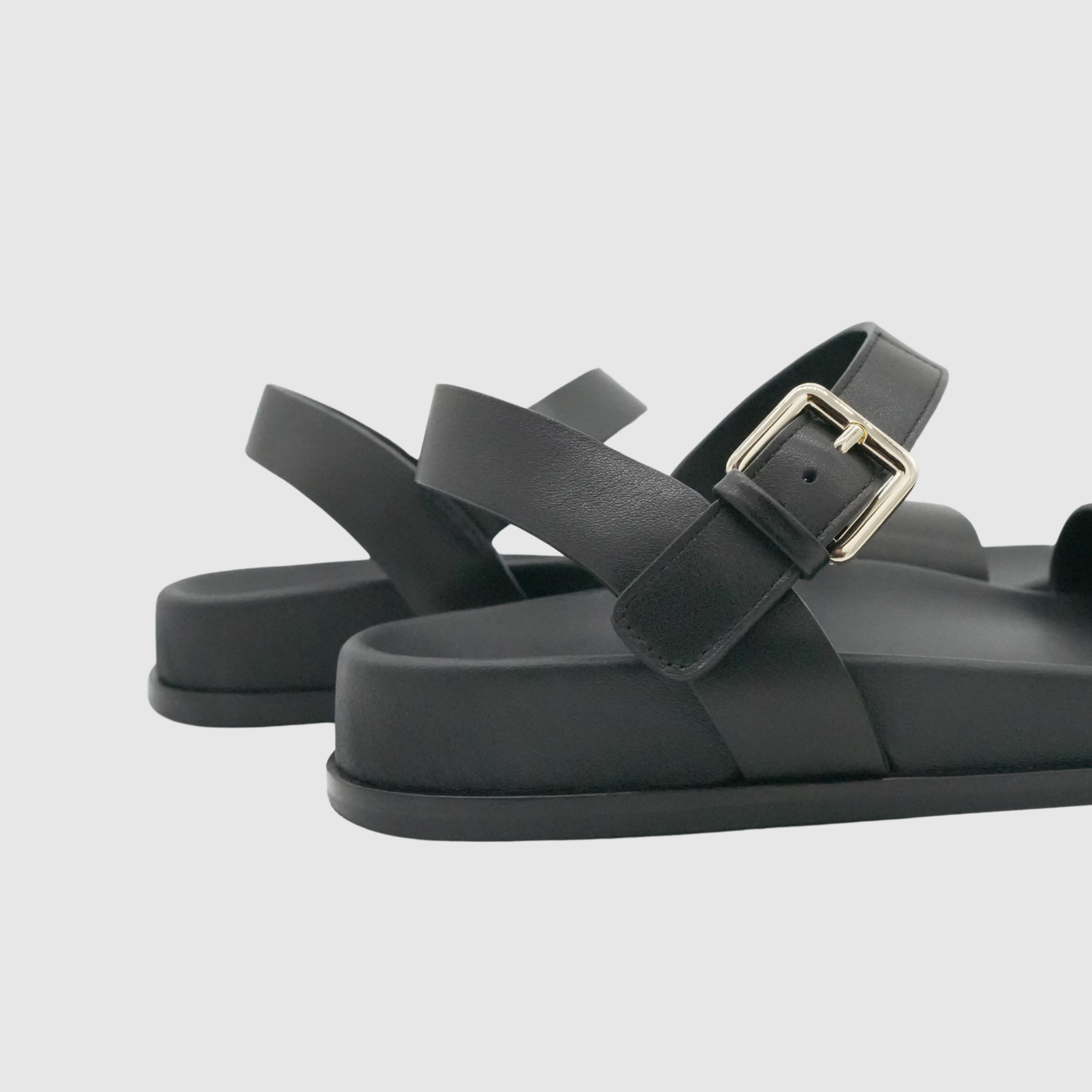 Black sandals with a gold buckle on a light gray background