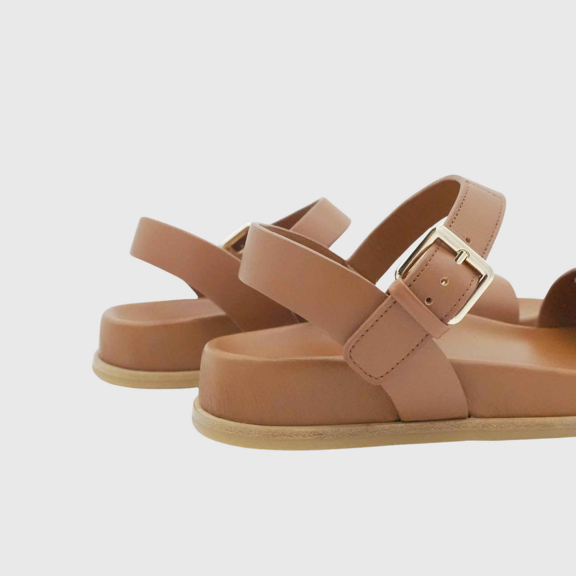 Pair of brown sandals with a gold buckle on a light gray background